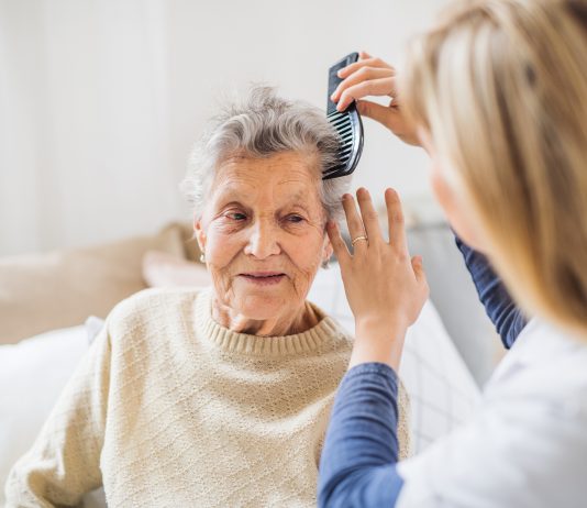 A health visitor combing hair of senior woman at home..