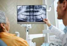 Back view closeup of male dentist pointing at teeth X ray image on screen