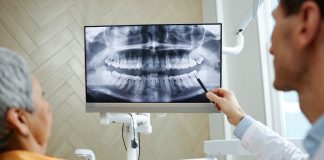 Back view closeup of male dentist pointing at teeth X ray image on screen