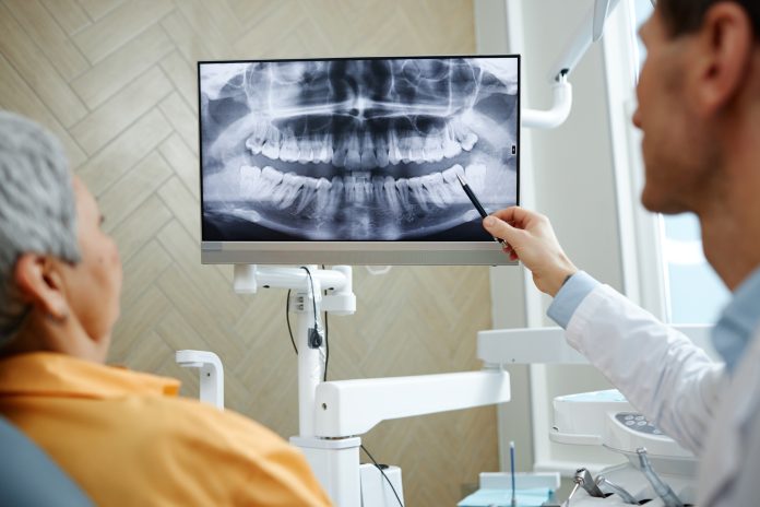 Back view closeup of male dentist pointing at teeth X ray image on screen