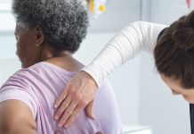 Diverse female doctor testing back of senior female patient in hospital room. Medicine, healthcare and medical services, unaltered.