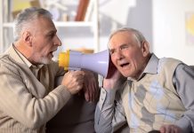 Senior man shouting bullhorn to deaf friend, old aged health, deafness treatment