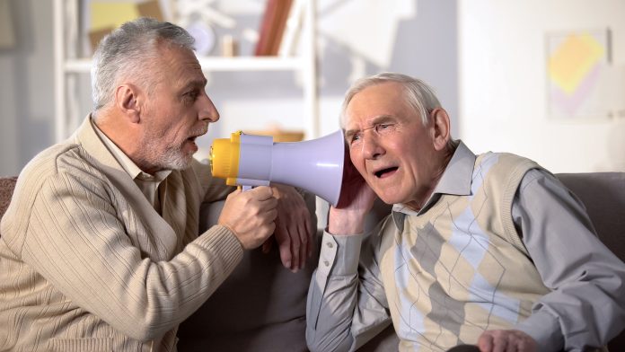 Senior man shouting bullhorn to deaf friend, old aged health, deafness treatment