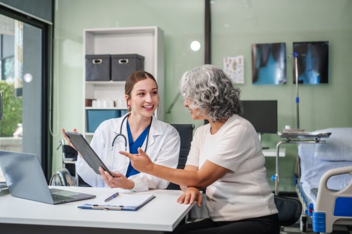 Monthly health check ups and counseling sessions are provided to an elderly Asian woman by a Caucasian female caregiver, offering support, advice, and motivation.